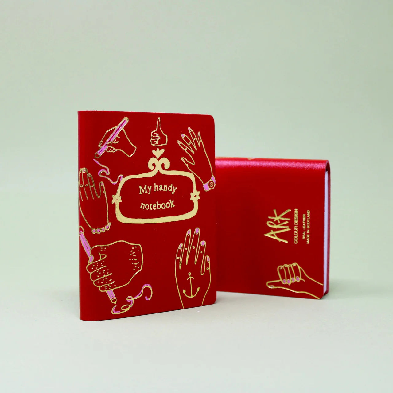 A small red notebook with gold accents on the front. The text reads: My handy notebook 