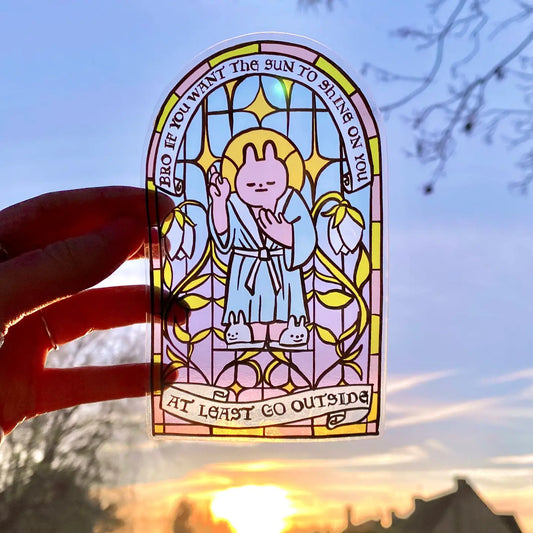 A transparent stained glass inspired sticker with a bunny design, held against a sunset background.