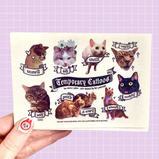 A hand holding a sheet of temporary tattoos featuring various cats.