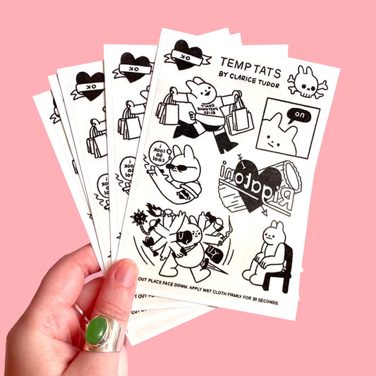 Hand holding a sheet of black and white tattoo designs on a pink background