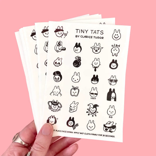 Sheet of Tiny Tats by Clarice Tudor temporary tattoos held against a pink background