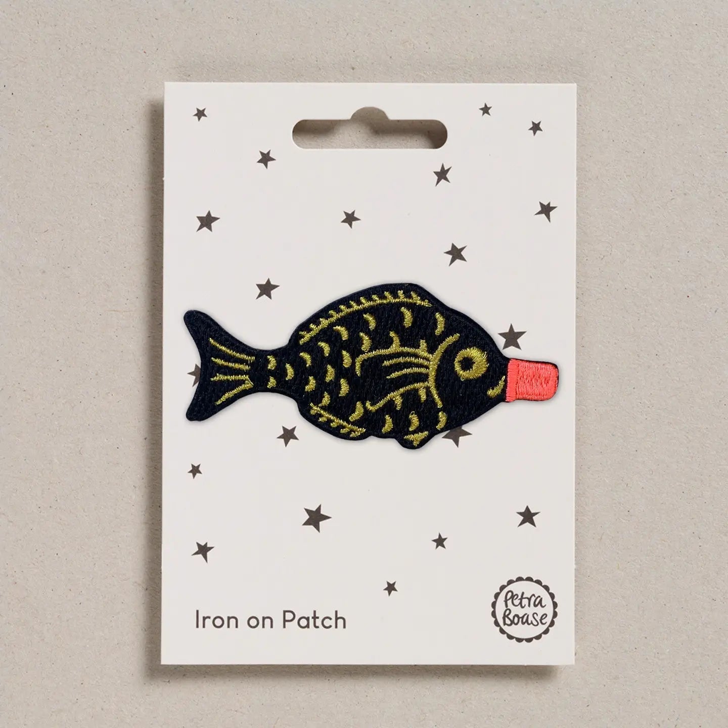 Fish-shaped iron on patch on a white card with star patterns, brand 'Petra Boase' visible.