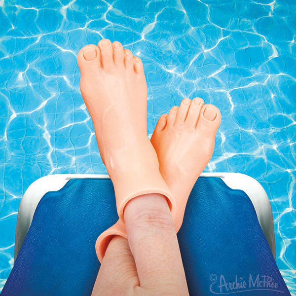 A pair of Archie McPhee finger feet on someone’s fingers pretending they are relaxing on a sunbed by the pool. 