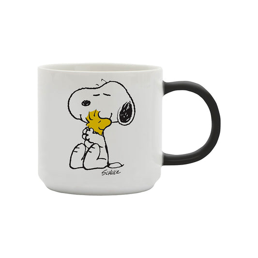 A white mug with a black handle. On the front of the mug is a graphic of Snoopy hugging Woodstock.