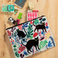 A white Blue Q zipper pouch with 3 black cats on the front and blue, green, yellow and pink floral print all over.