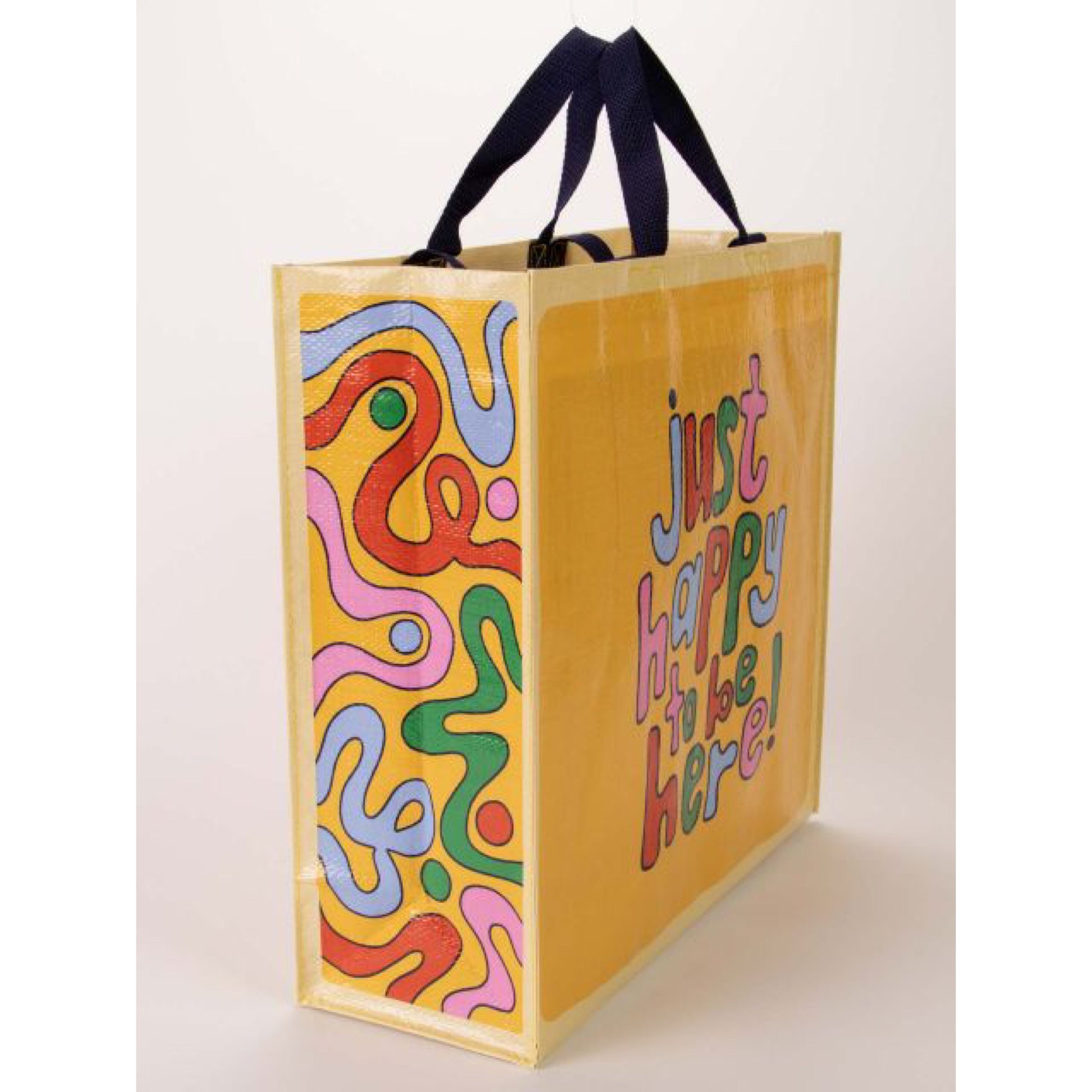 A yellow Blue Q tote bag with Blue, green, red and pink squiggles on the side. The text reads: Just happy to be here!