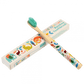 A wooden toothbrush with wild animal images on the handle is leaning up against a white cardboard box that reads: Faries in the garden bamboo toothbrush. 