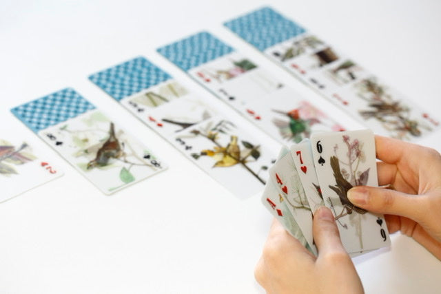 Someone holding 4 lenticular bird playing cards with a game of solitaire set out on the table.