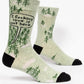 This image shows a pair of green men's socks with little trees on them. There is a speech bubble on them that reads i fucking love it out here