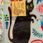 A white Blue Q lunch bag with a drawing of a black cat with pink blue yellow and green around. 