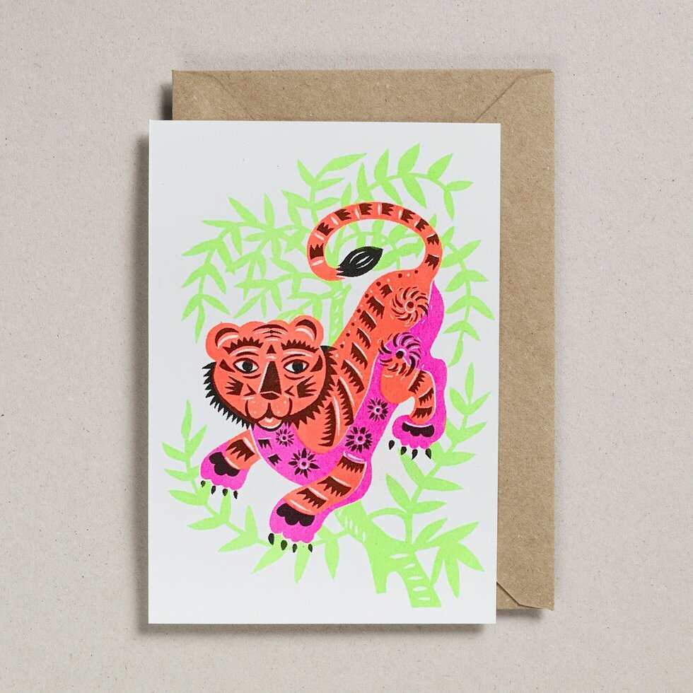 A white card with an orange tiger printed on the front. The tiger has a pink belly and nice patterns all over with some green laves behind.