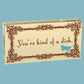 Beige box of Blue Q gum with a fancy brown boarder and a blue butterfly. The text reads: You're kind of a dick
