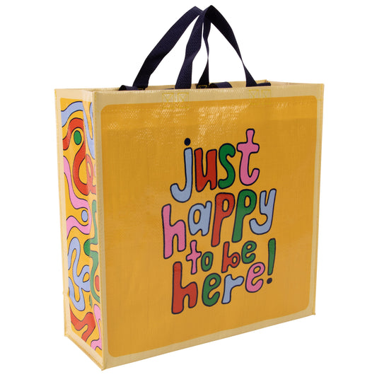 A yellow Blue Q tote bag with Blue, green, red and pink squiggles on the side. The text reads: Just happy to be here!