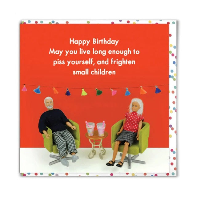 This image shows a birthday card with the image of a cartoon elderly couple sat on chairs with some drinks in the middle of them. The text on the card reads 'Happy Birthday May you live long enough to piss yourself, and frighten small children.' The cards is red with some colourful bunting in the background and there is a spotty envelope 