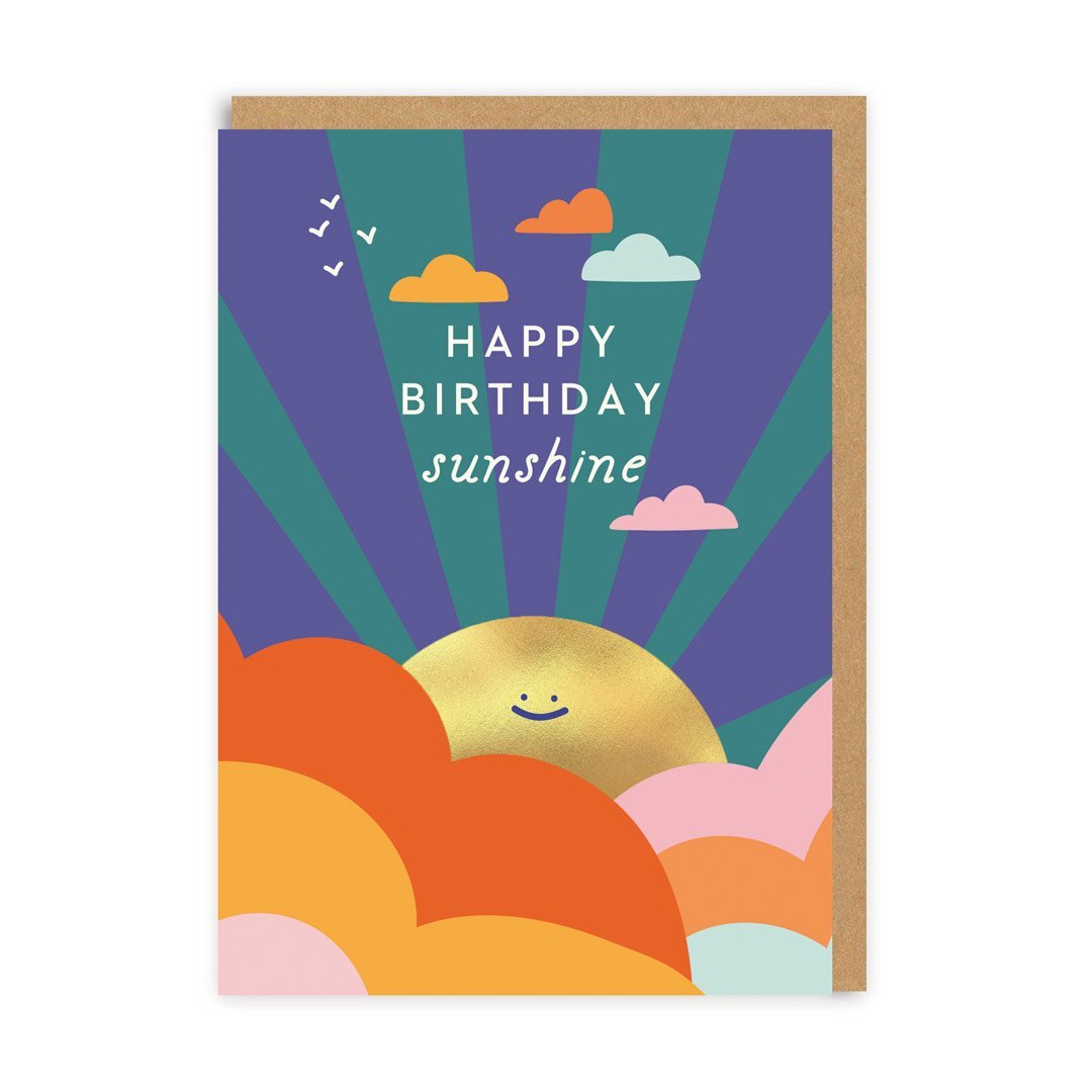 A blue card with orange yellow and pink clouds at the bottom and a golden smiling sun peaking out from behind them. The text on the card reads: Happy birthday sunshine 