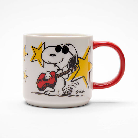 A white mug with a red handle. On the front of the mug is a graphic of Snoopy playing the guitar with sunglasses on and all around him are big yellow stars  