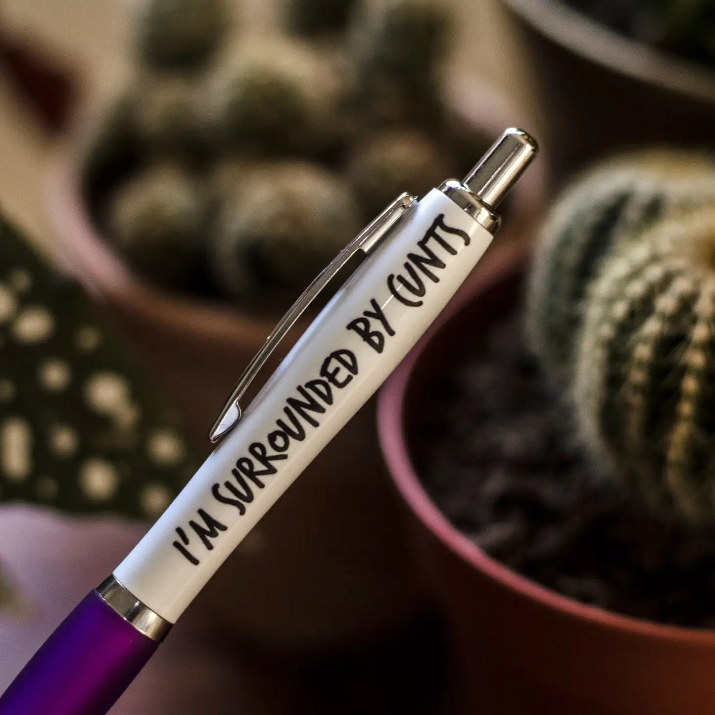 A white and purple coloured pen that reads: I'm surrounded by cunts