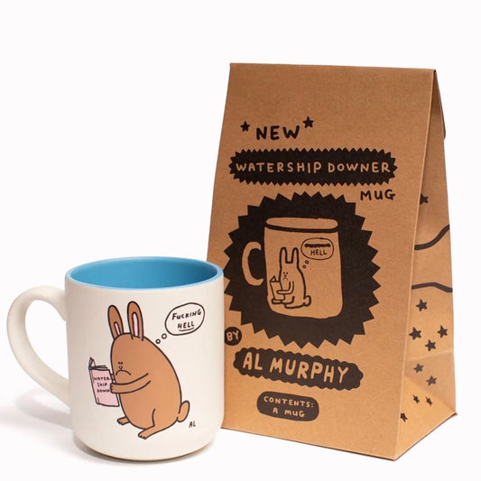 A white mug with blue on the inside. On the outside of the mug is a cartoon illustration of a rabbit reading Watership Down. There is a thought bubble coming from the rabbit that reads: ' Fucking HELL'