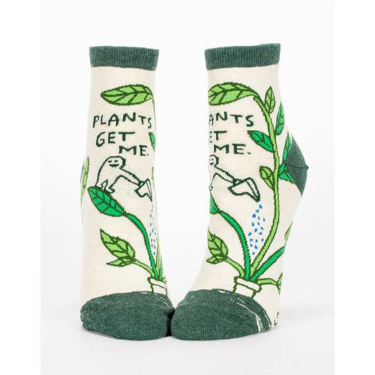Beige and green Blue Q socks with a little character on the front watering a plant. The text reads ‘plants get me’