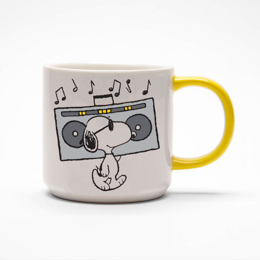 A white mug with a yellow handle. On the mug is a graphic of Snoopy carrying a stereo on this shoulder with sunglasses on.