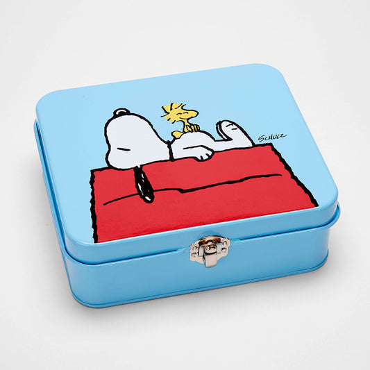 A blue tin with a silver clasp on the front. On the tin is a graphic of Snoopy sleeping on top of the shed with Woodstock on his belly.