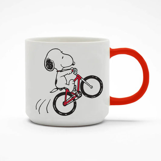 A white mug with a red handle. There is a graphic on the mug of Snoopy doing a wheelie on a bike
