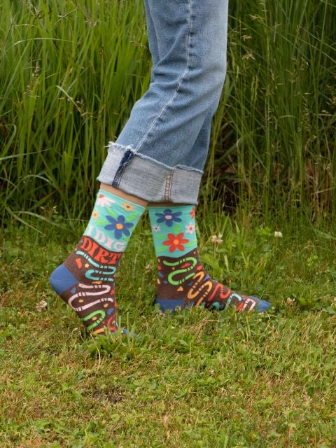 Blue Q 'I dig dirt' socks being worn by someone whilst they stand outside on the grass 