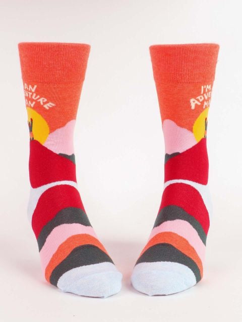 Image shows orange and red men's socks with a graphic of a man walking over a mountain with the sun behind with text above says i'm an adventure man