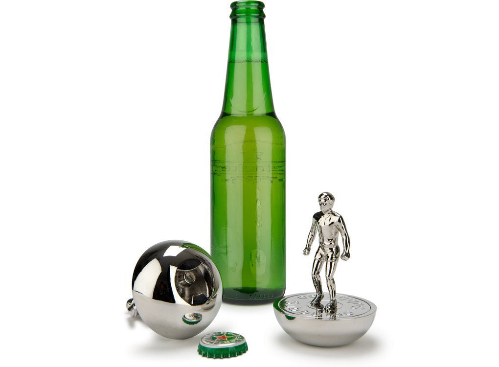 Two Subbuteo bottle openers, one on it's side and one standing up, in front of a green bottle