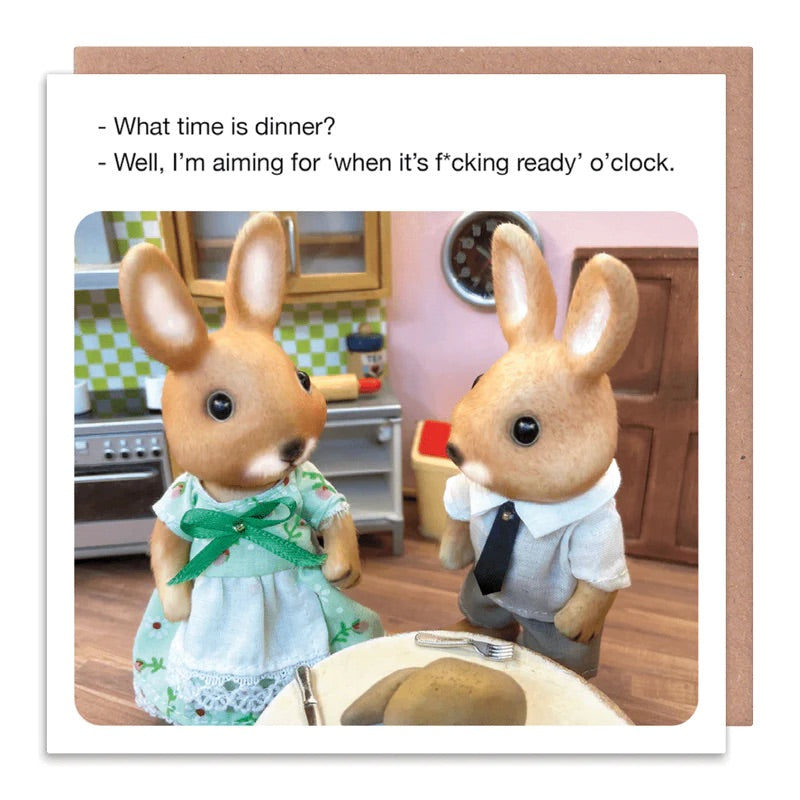 A white card with 2 rabbits stood in the kitchen. The text on the card reads: What time is dinner? - Well, i'm aiming for 'when it's f*cking ready' o'clock.