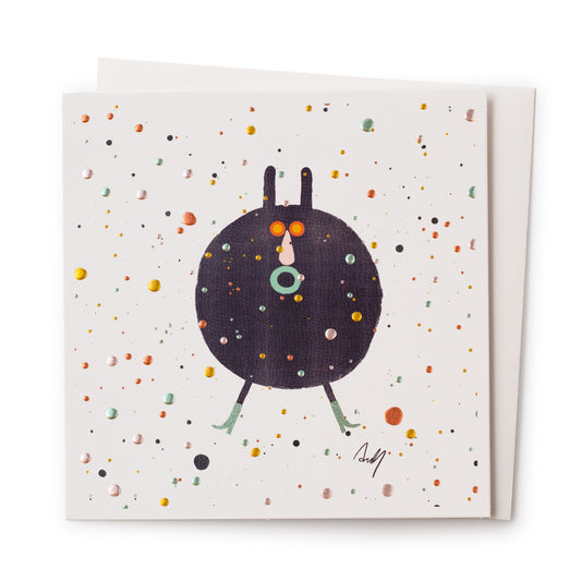 A white card with a picture on the front of a space hopper with a shocked face and legs. Around him all over the card are gold, bronze, blue, green and white metallic dots. 